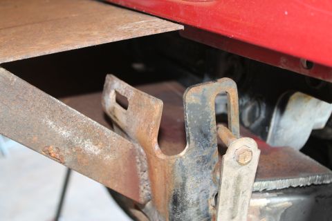 1990 Ford Bronco - Detail of a corroded metal bracket and part of a red body panel, showing signs of wear.