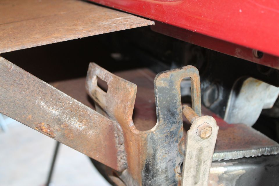 Close-up of a rusty metal bracket attached to a red panel, with a bolt visible