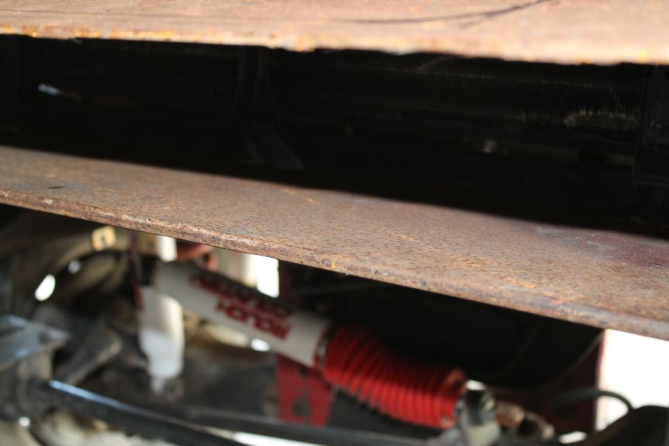 Undercarriage of a vehicle with a rusty metal plate and a white and red shock absorber with a red boot