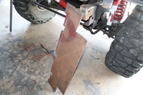 1990 Ford Bronco - Metal plates and tools are laid out on the floor, suggesting custom bumper fabrication work near the suspension and tire of a vehicle.