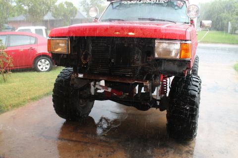 1990 Ford Bronco - A lifted red truck sits in the rain, showing off its massive tires and suspension modifications.
