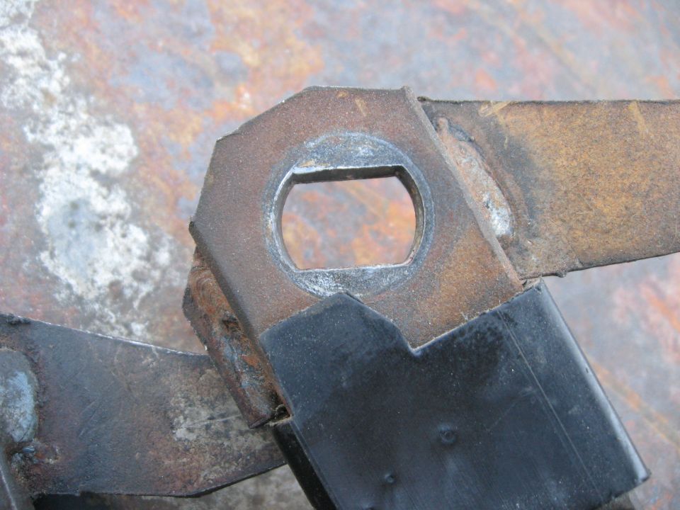 Close-up of a rusty metal bracket with a hexagonal opening, possibly part of a vehicle's drivetrain or suspension
