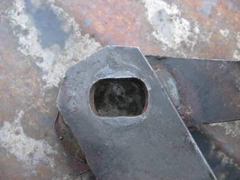 1981 Ford Bronco - Close-up of a metal bracket with a cutout, likely a vehicle part, on a rusty surface.