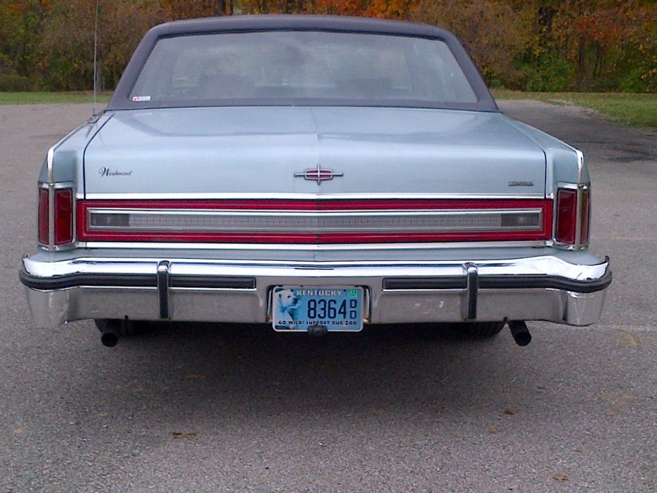 Rear view of a light-colored sedan with a chrome bumper and a blue license plate