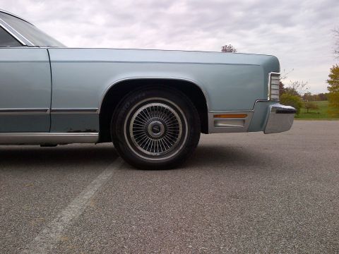 2001 Ford Crown Victoria - Side view of a light blue sedan's front end, showing the wheel and bumper details.