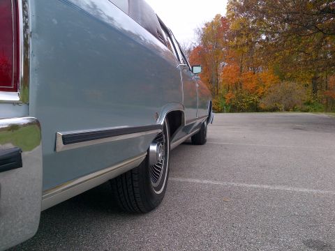 2001 Ford Crown Victoria - A light blue Cadillac Sedan de Ville is parked outdoors with autumn trees visible in the background.