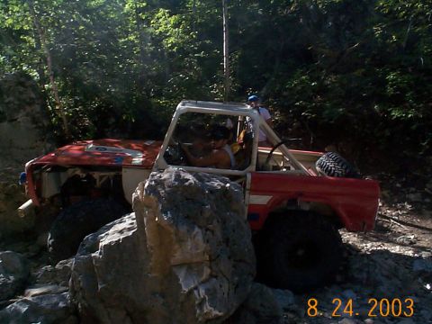 1977 Ford Bronco - This modified off-road vehicle is shown tackling a challenging rocky path in a wooded area.