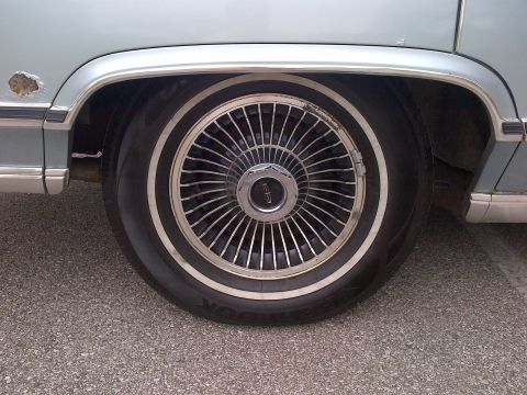 2001 Ford Crown Victoria - A close-up of a car's wheel and fender reveals rust damage and a distinctive hubcap.