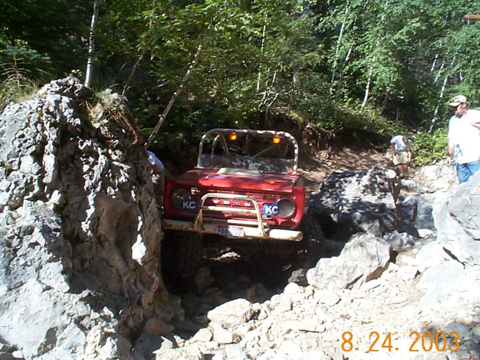 Red 1977 Ford Bronco off-roading on a rocky trail, front view