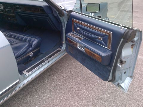 2001 Ford Crown Victoria - The interior of a classic car features plush blue quilted seats and elegant wood trim accents on the door panel.