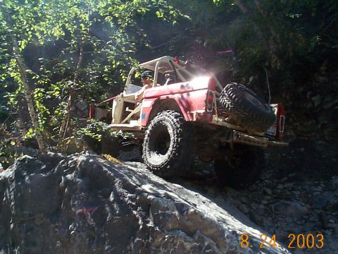 1977 Ford Bronco - Modified 1977 Ford Bronco tackling a steep, rocky trail with a driver visible.