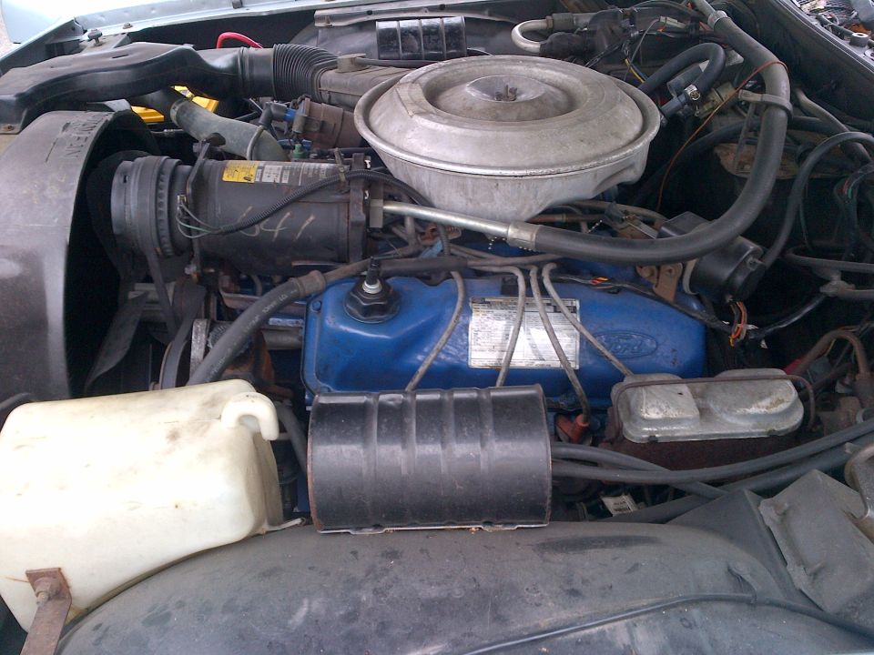 engine bay with blue Ford valve covers, air cleaner, and AC compressor