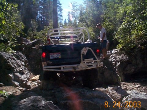 1977 Ford Bronco - This vehicle navigates a challenging rocky trail surrounded by dense forest.