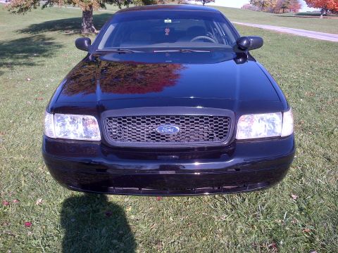 2001 Ford Crown Victoria - Front view of a black 2001 Ford Crown Victoria parked on a grassy area with trees and a road in the background.