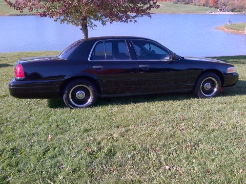2001 Ford Crown Victoria - A black 2001 Ford Crown Victoria is seen from the side, parked on a grassy area next to a body of water.