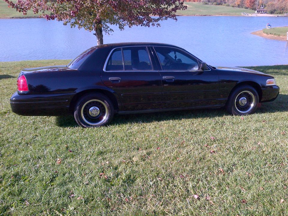 Side view of a black 2001 Ford Crown Victoria parked on grass by a lake