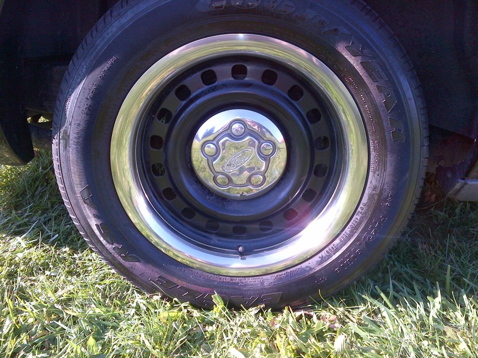 Black steel wheel with chrome trim and Ford hubcap on grassy ground