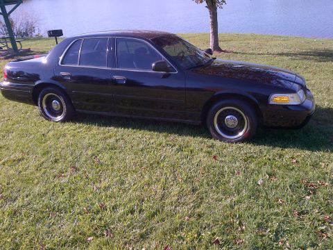 2001 Ford Crown Victoria - A black 2001 Ford Crown Victoria is parked on a grassy area next to a body of water.