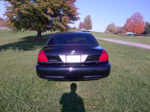 2001 Ford Crown Victoria - Rear view of a black sedan parked on a grassy hill under a clear blue sky.