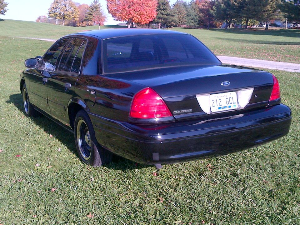 Black 2001 Ford Crown Victoria with a license plate reading 212 GCL parked on grass