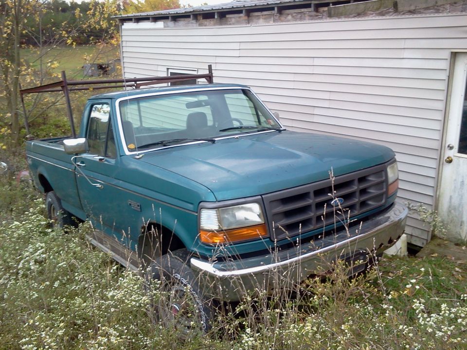 1994 Ford F-350 pickup truck parked in overgrown grass next to a building