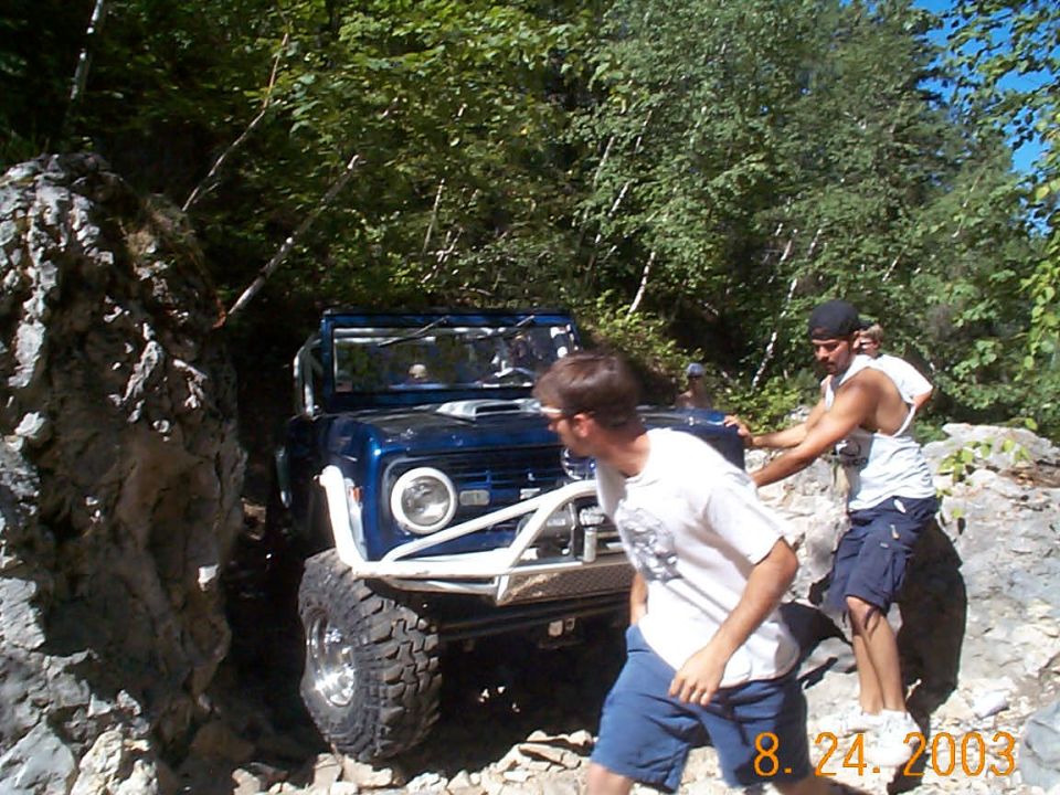 Blue off-road SUV with a white roll cage and large tires navigating a rocky trail