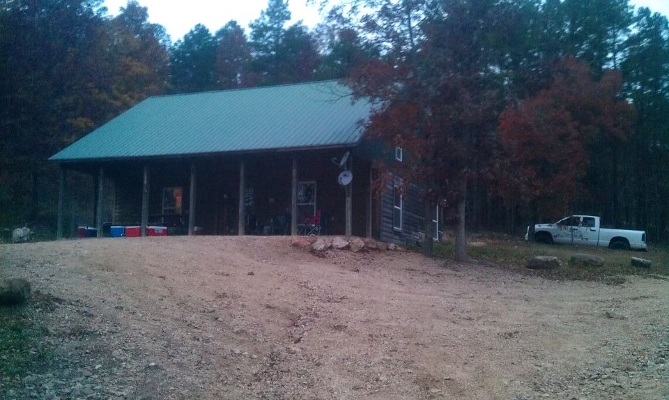 White pickup truck parked on grass next to a cabin in the woods