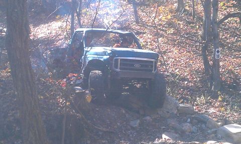 1987 Ford Bronco - A blue Ford truck navigates a challenging rocky terrain on an off-road trail.
