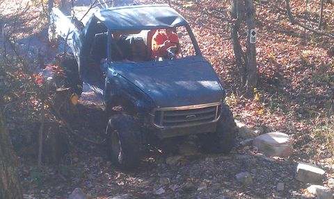 1987 Ford Bronco - This heavily modified truck navigates a challenging off-road course, its roof showing signs of damage from the trail.