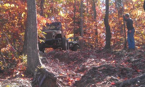 1987 Ford Bronco - Off-road vehicles navigate a challenging trail surrounded by trees in autumn colors.