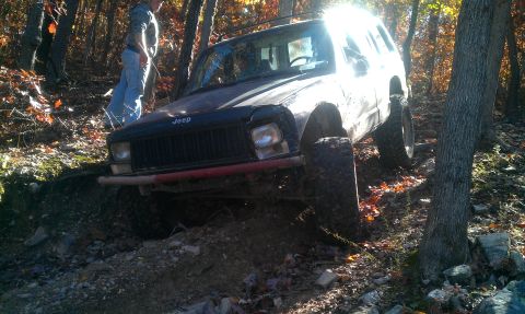 1987 Ford Bronco - A Jeep Cherokee navigates a challenging off-road trail surrounded by autumn foliage.