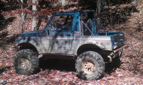 1987 Ford Bronco - This off-road vehicle is covered in mud and parked in a wooded area during autumn.