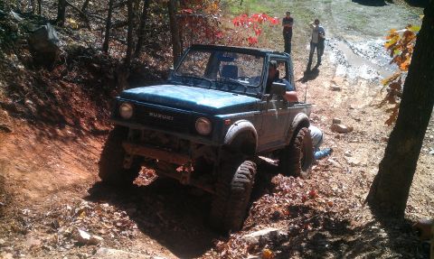1987 Ford Bronco - A Suzuki Samurai navigates a muddy, wooded trail during an off-road excursion.