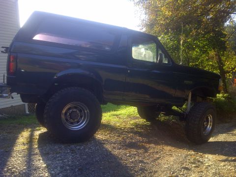 1995 Ford Bronco - This lifted 1995 Ford Bronco features oversized tires and a dark blue exterior, captured in a three-quarter front side profile.