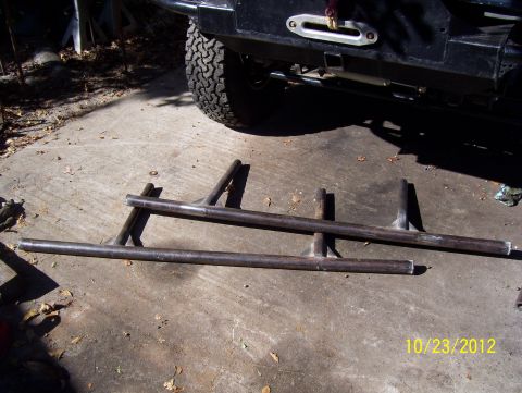 1990 Ford Bronco - Custom fabricated metal parts laid out on concrete, with a vehicle tire and bumper in the background.