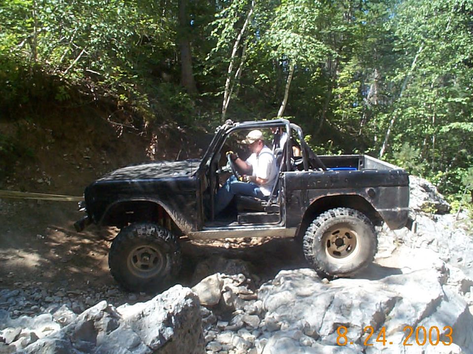Black 1977 Ford Bronco off-roading on a rocky trail, driver visible