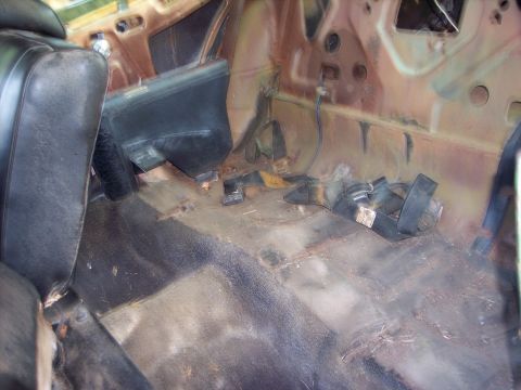 1970 Chevrolet Chevelle - The interior of a car shows significant wear and tear, with rusted metal and dirty flooring visible.