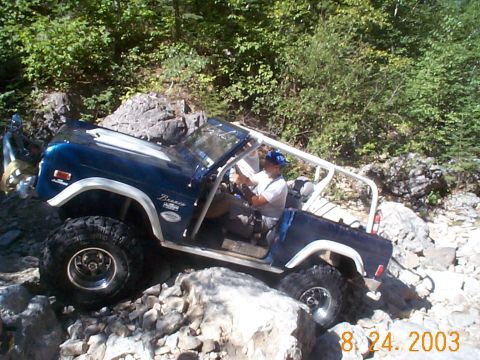 1977 Ford Bronco - A blue 1977 Ford Bronco navigates a rocky trail, demonstrating its off-road capabilities.