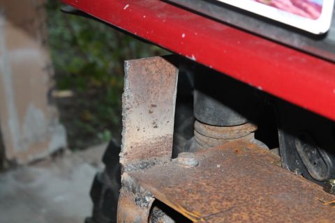 1990 Ford Bronco - Close-up view of a rusted metal bracket attached to the red body of a vehicle.