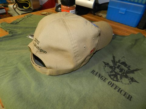 1996 Ford Bronco - A tan baseball cap and green t-shirt are laid out on a wooden surface. The cap has '2012 Multigun' embroidered on it.