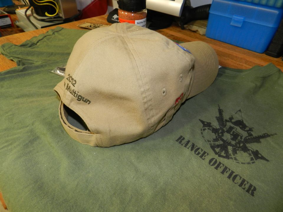 Tan baseball cap with '2012 Multigun' embroidered on the back, resting on a green t-shirt with 'RANGE OFFICER' and a graphic