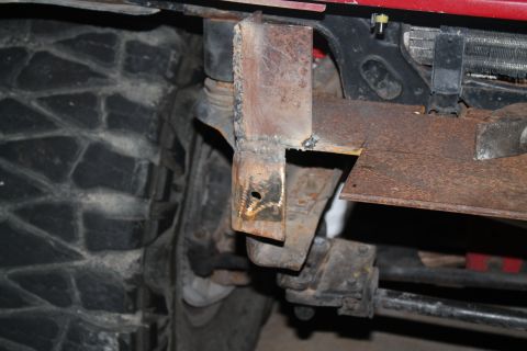 1990 Ford Bronco - A close-up view of a heavily rusted metal bracket attached to a vehicle's frame, with a tire visible to the left.