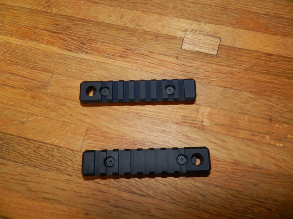 Two black Picatinny rails with screws on a wooden surface