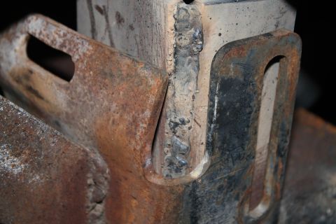 1990 Ford Bronco - This is a close-up view of a rusty metal bracket with visible welds, likely part of a vehicle's frame or bumper assembly.