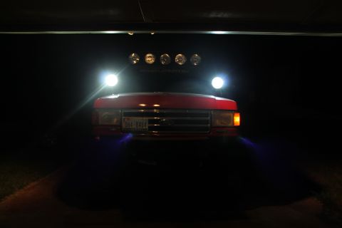 1990 Ford Bronco - Front view of a red 1990 Ford Bronco at night, illuminated by its headlights and a row of roof-mounted lights.