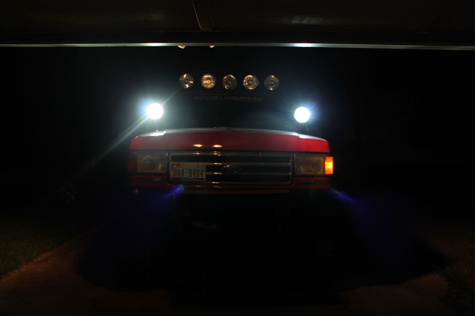 Red 1990 Ford Bronco front with headlights and roof lights on