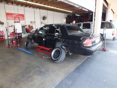 2003 Ford Crown Victoria - Rear view of a black sedan raised on a shop lift; jack stands and an air line sit on the floor.