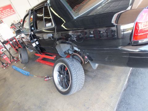 2003 Ford Crown Victoria - Side rear view of a black sedan on a lift; mounted black wheel with polished outer lip in foreground.