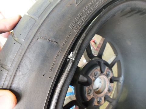 2003 Ford Crown Victoria - Detail of a tire sidewall showing a crack near a black wheel and a rusted hub in a garage.