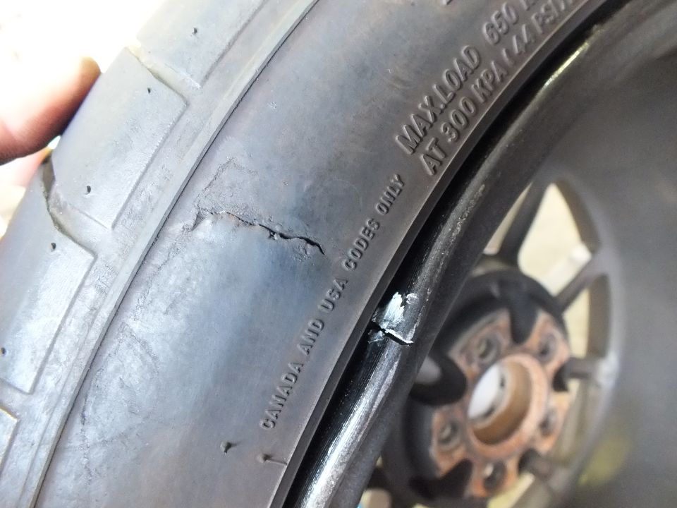 Close-up of cracked tire sidewall with stamped text near a black wheel and rusty hub